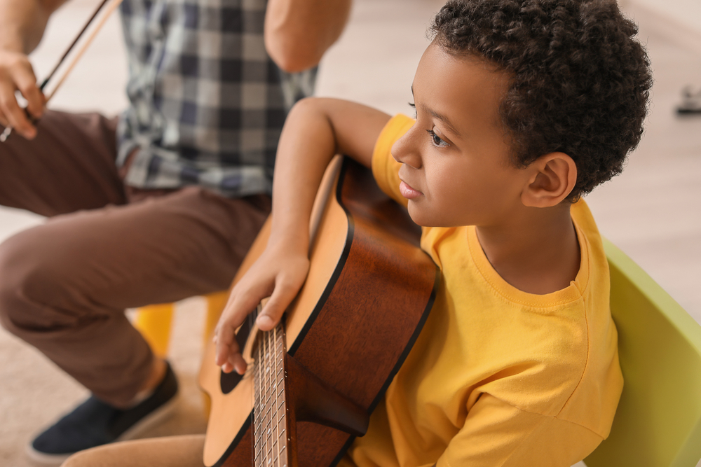 A young student holding an acoustic guitar during a lesson