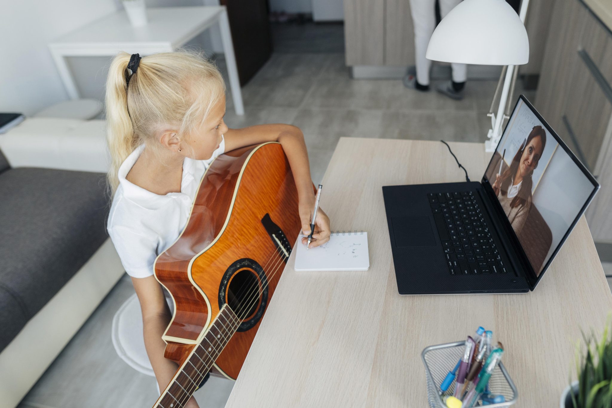 A student holding a guitar during a live video music lesson at home